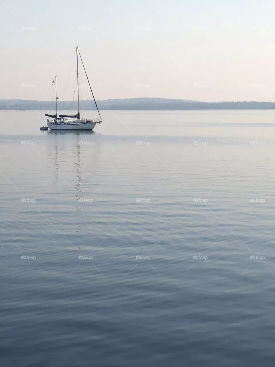Sail boat on water. Sky, boat, and water are all soft blue hues.