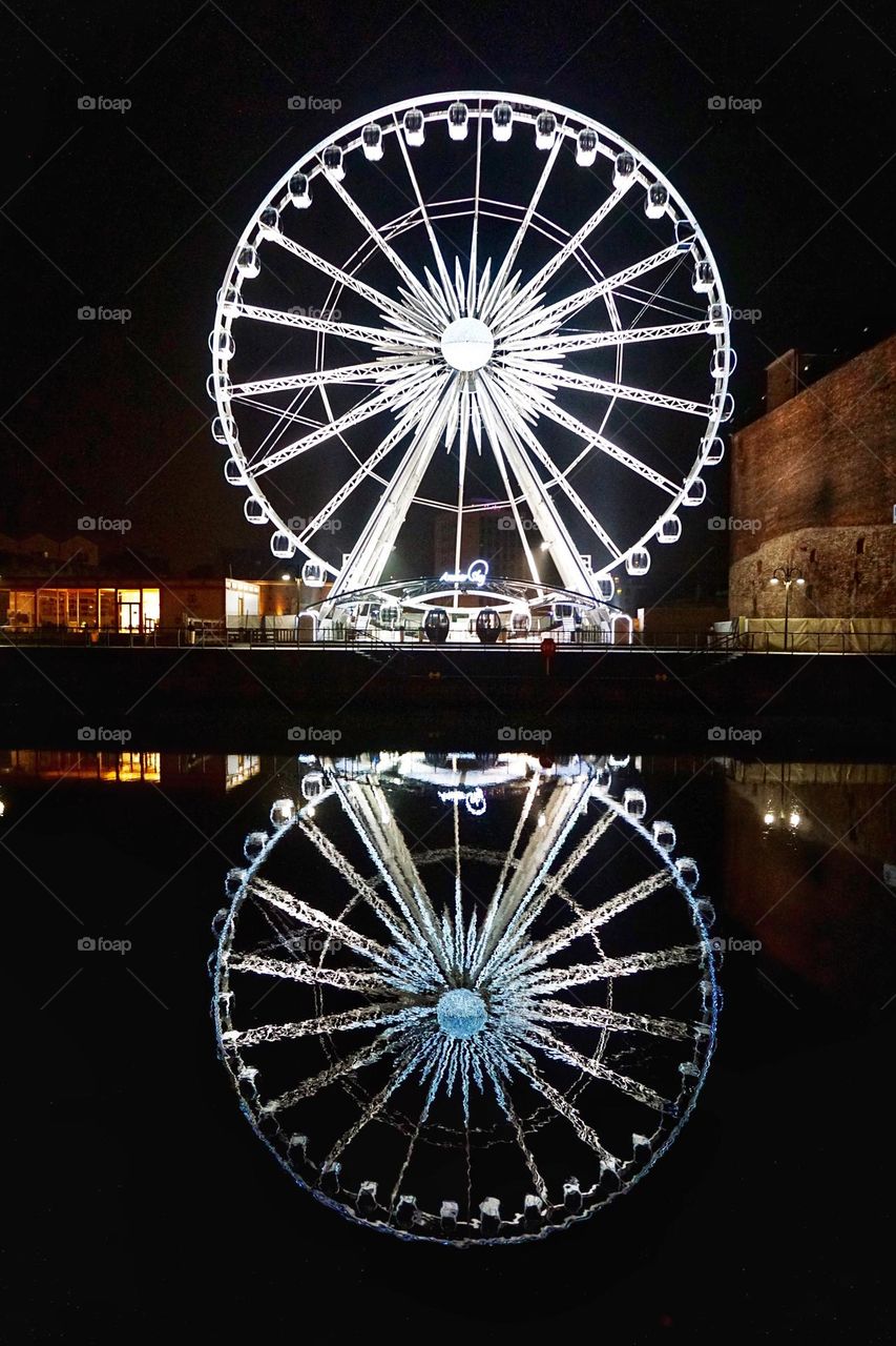 Ferris Wheel lit up at night with a full reflection in the water 