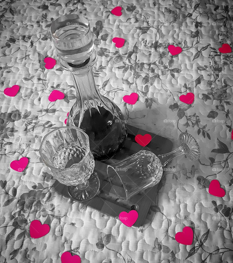 Two glasses and decanter with wine on the bed with hearts.