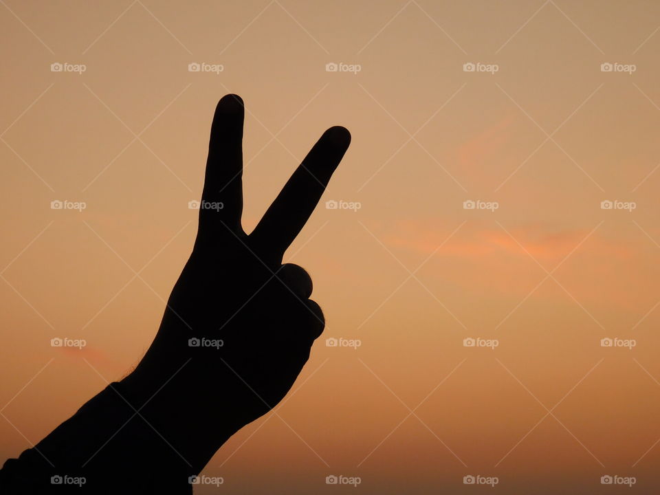 Victory symbol with hand posture having sunset light background.It is silhouette image.