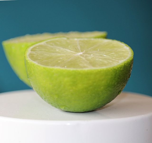Juicy organic green lime halves still life on teal blue background, concept citrus fruit, vitamin C, cold remedy, health and nutrition, copy space