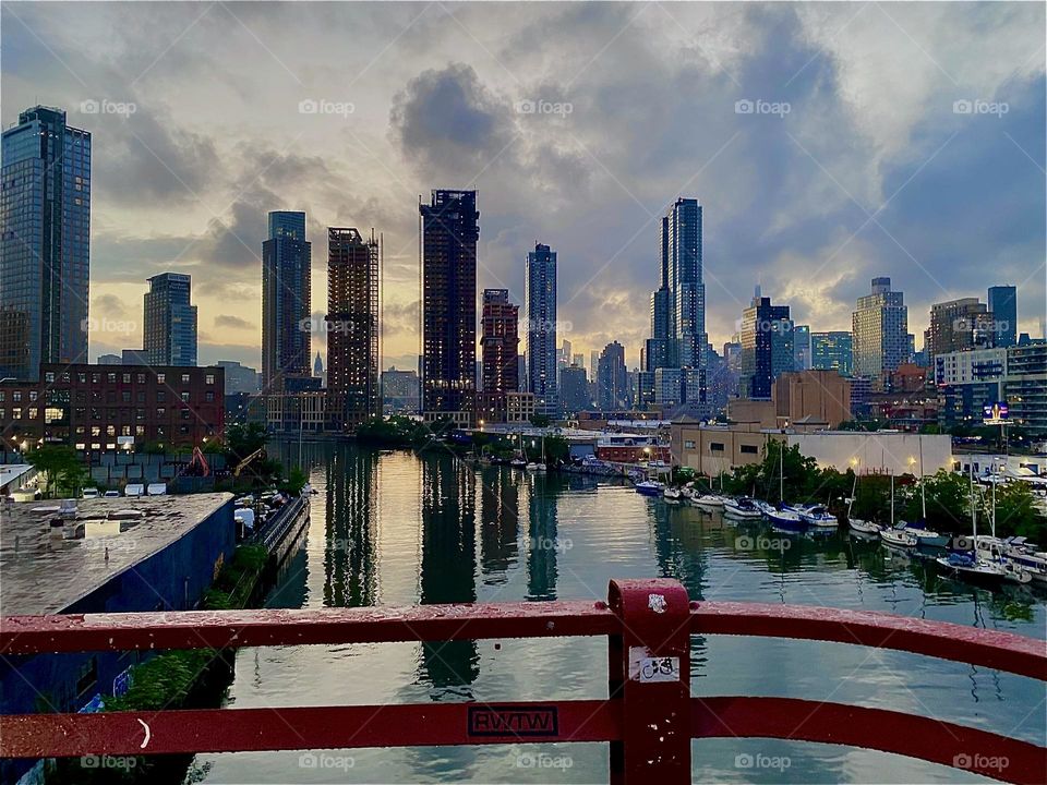 Across the railing of the „Pulaski Bridge“ we can see „Newtown Creek“ and three boroughs of NYC: „Greenpoint“, Brooklyn to the left, „Queens“ to the right and straight ahead „Manhattan“. 2023. Hypnotic Productions