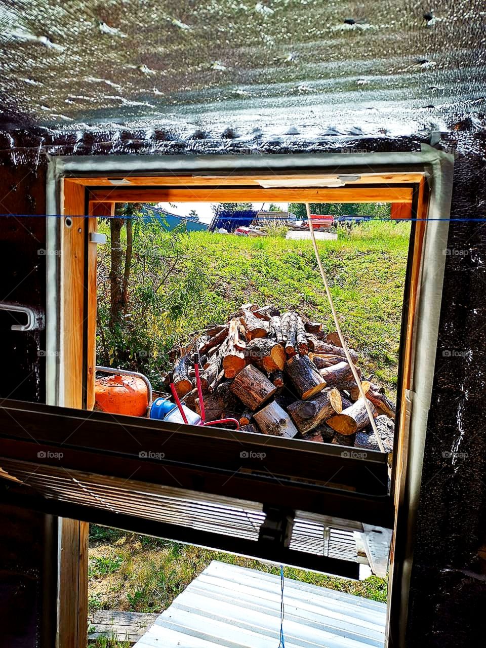 The window of the Russian bath through which green grass and logs on it are visible