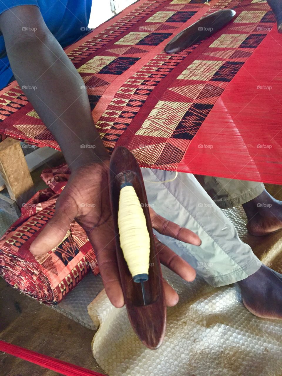 A weaver holds out his wooden shuttle while taking a break from making Manjak cloth 