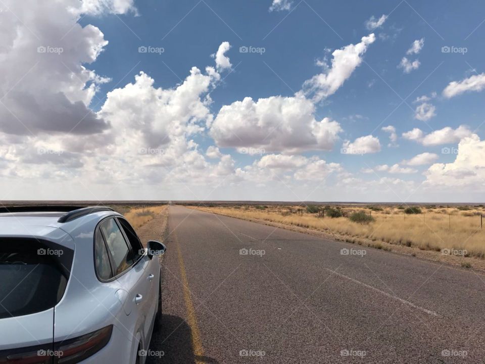 Image showing parts of a white Porsche on a road in the desert with a blue sky and some clouds.
