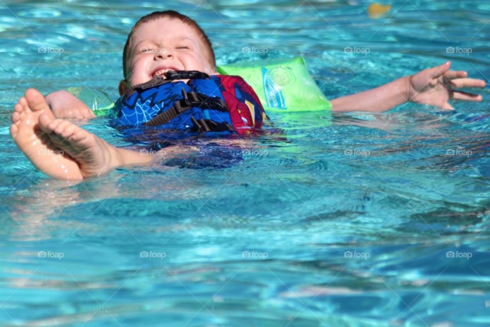 Little boy floating on water in swimming pool