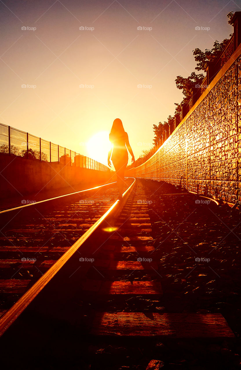 Woman is walking on a railways lit by the orange rays of the sunset