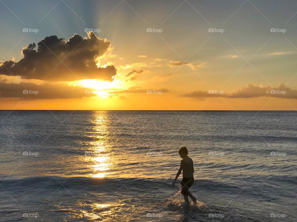 Beautiful landscape of a boy in an ocean sunset.