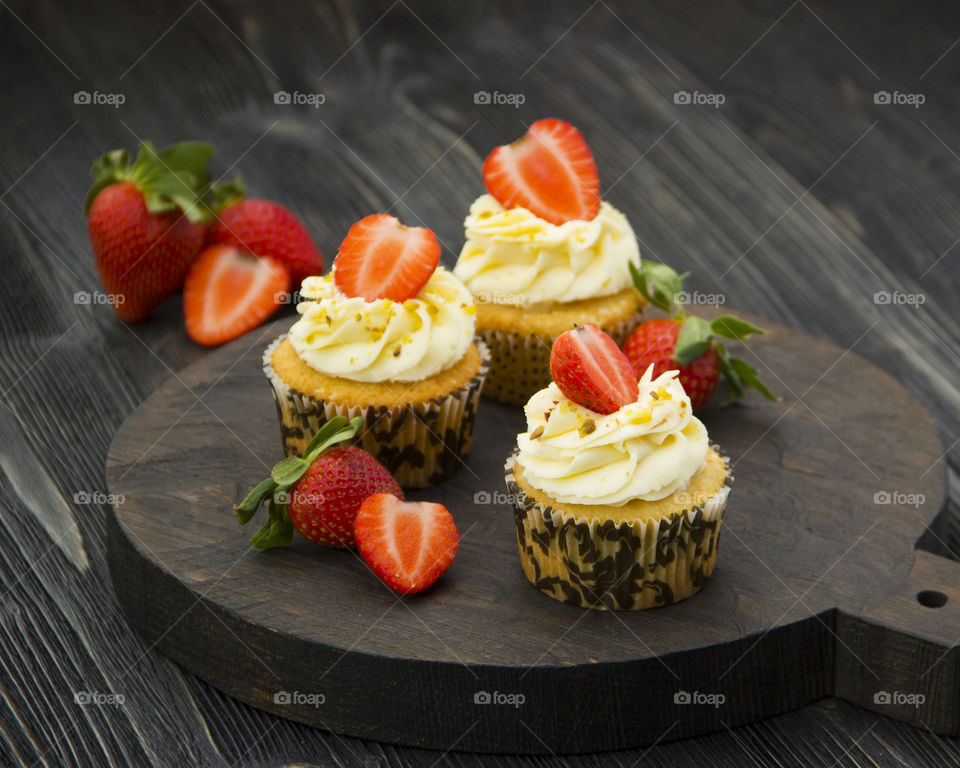Cupcakes with strawberries on wooden board.