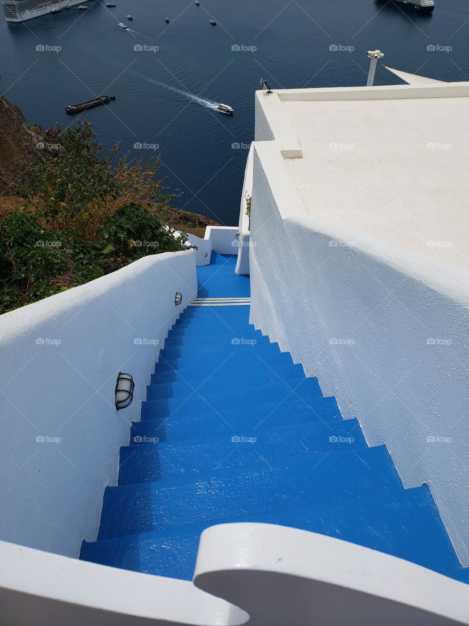 view from up high in Santorini, Greece, looking down a steep staircase towards the ocean and cruise ship
