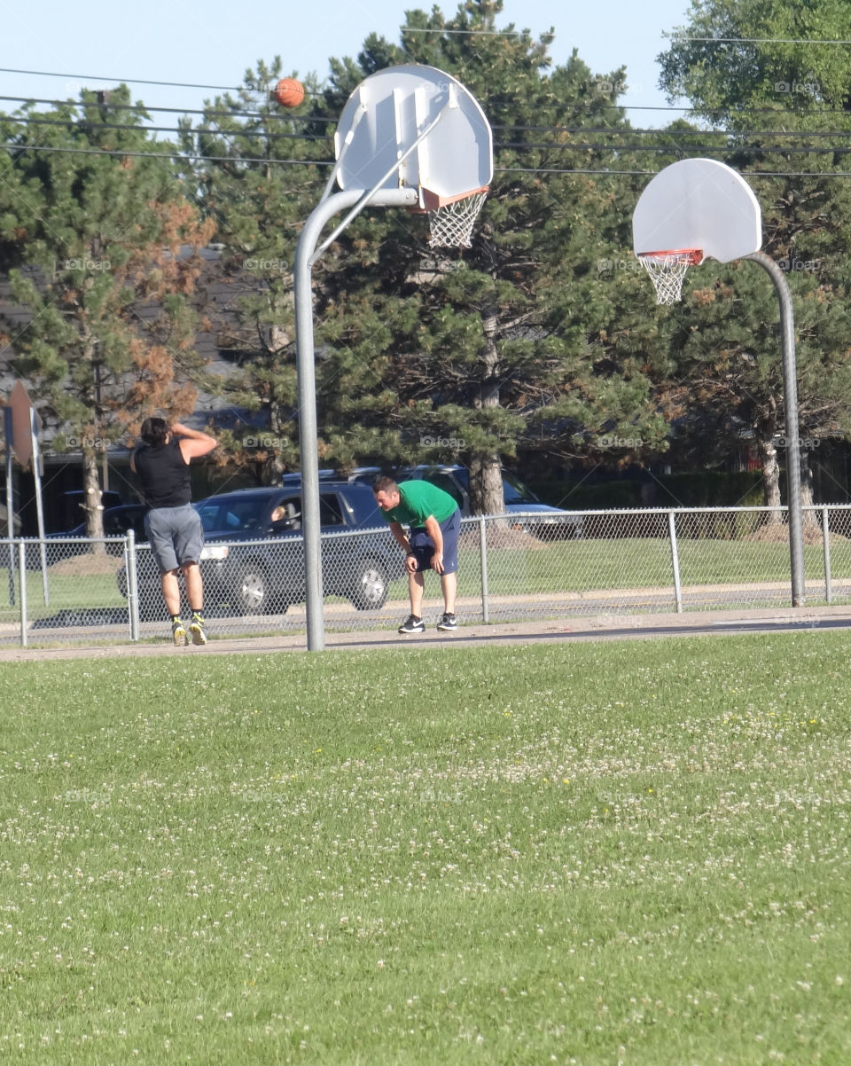 Jump Shot. Two men playing basketball outside, one man jumping, ball in mid air. 
