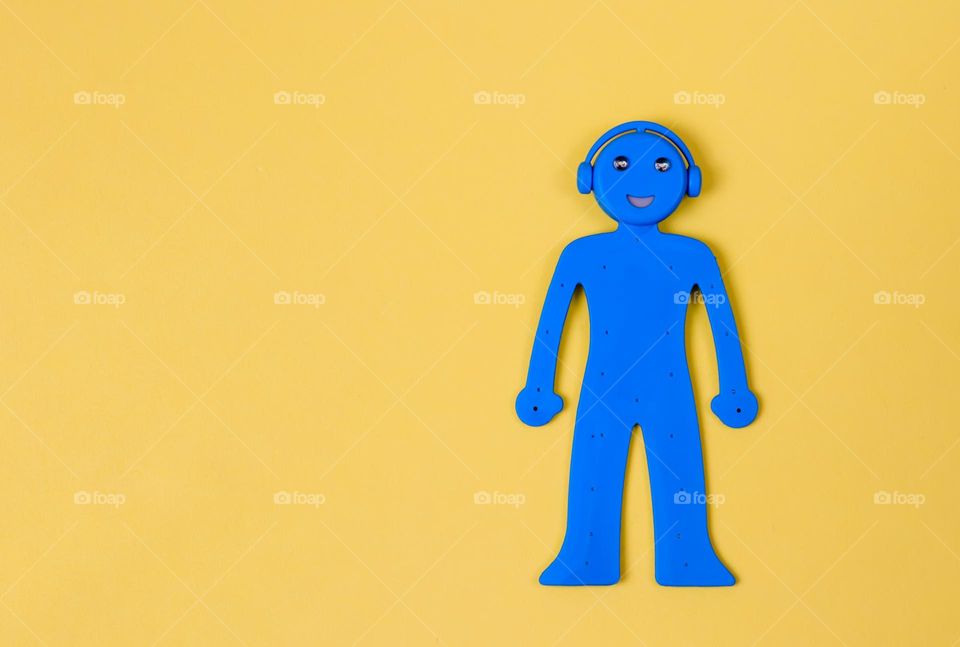 One rubber blue man with headphones flexible phone stand lies on the right on a yellow background with copy space on the left, flat lay close-up. Blue and yellow concept, modern accessories.