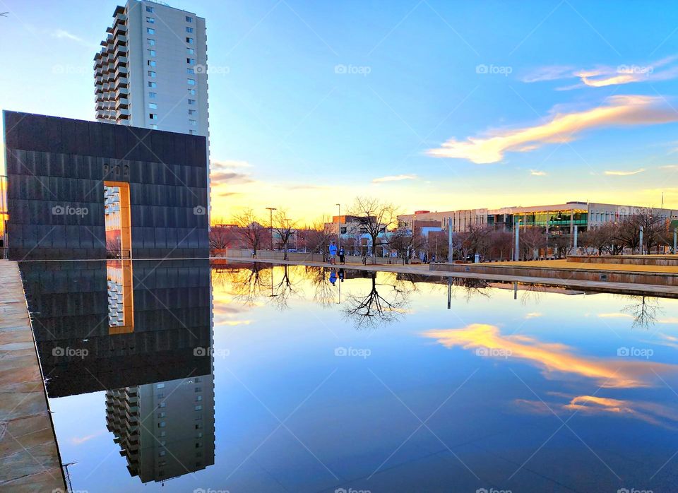 A memorial and a building are perfectly reflected in a shallow pool on a beautiful evening
