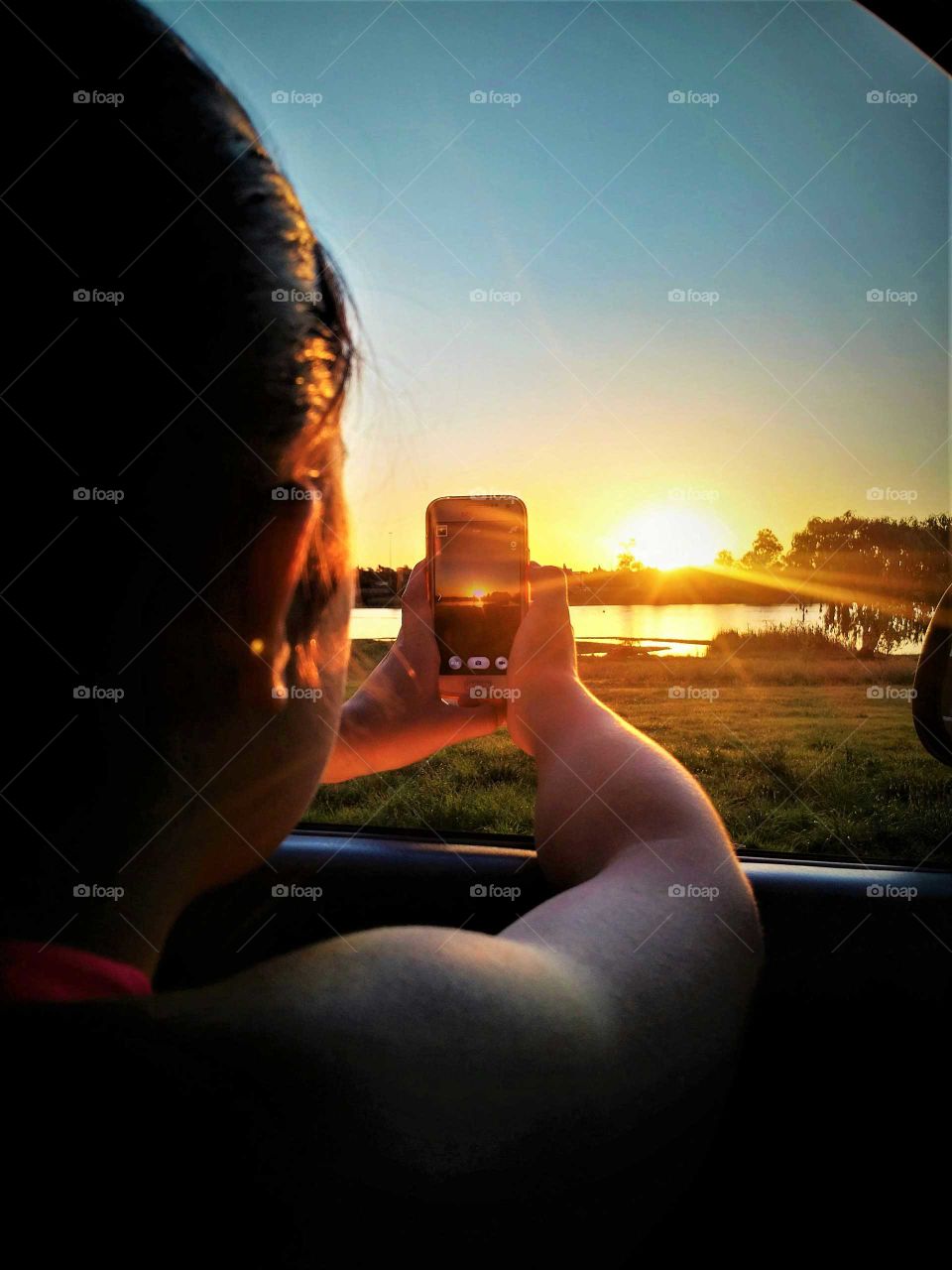 girl taking photograph of sunset with cellphone