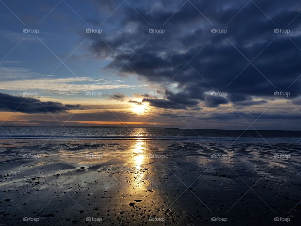 Beach at sunset, partial cloud and reflection on sand.