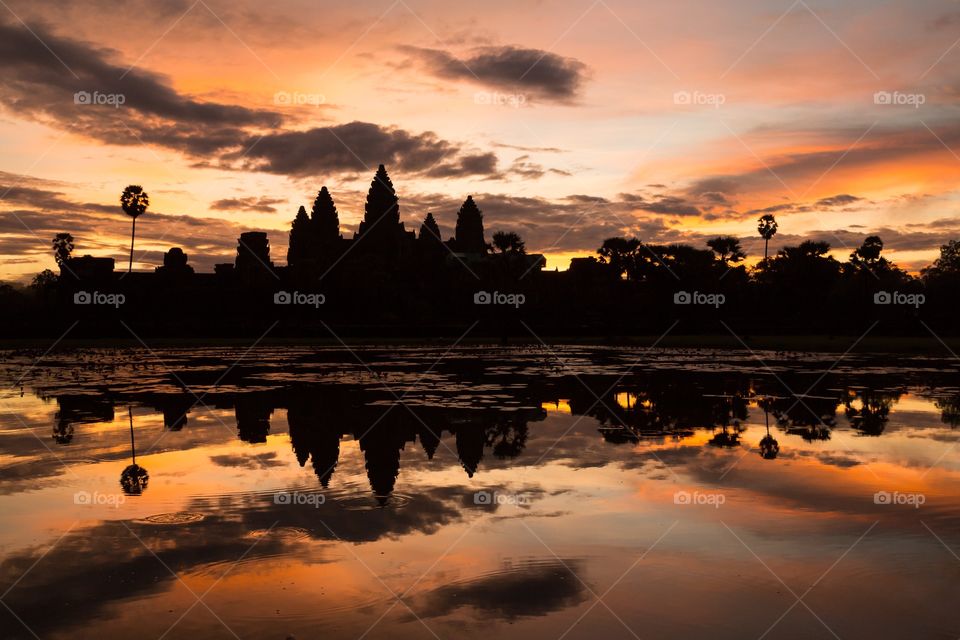 Angkor wat during sunrise. Angkor Wat during sunrise in backlit scene. Historical structure reflects from water. Silhouetted. Few clouds