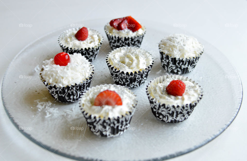 Mini cheesecakes in black and white decorative wrappers topped with whipped cream, coconut and berries