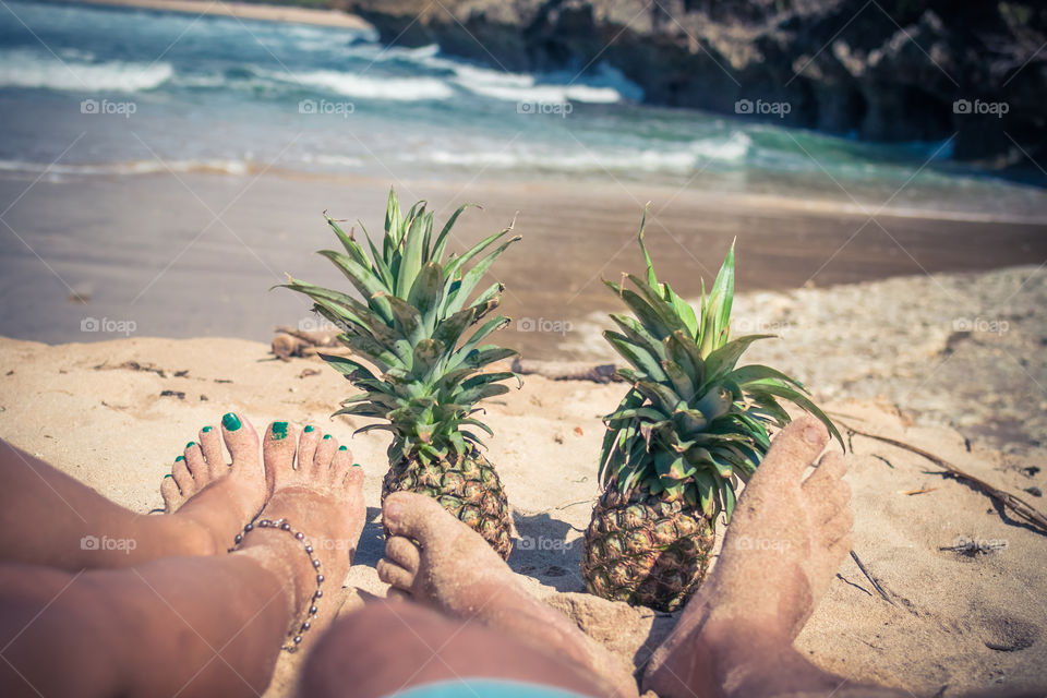 Couple sitting on the beach with pineapples. Bali island.