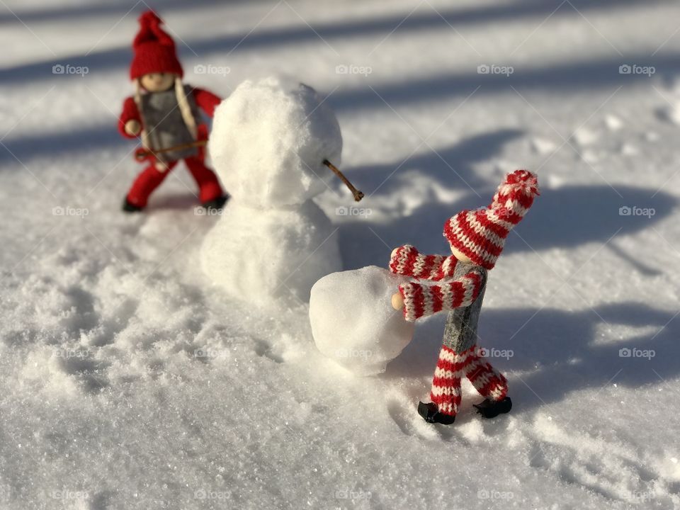 Two toy man building a snowman in the middle of white snow