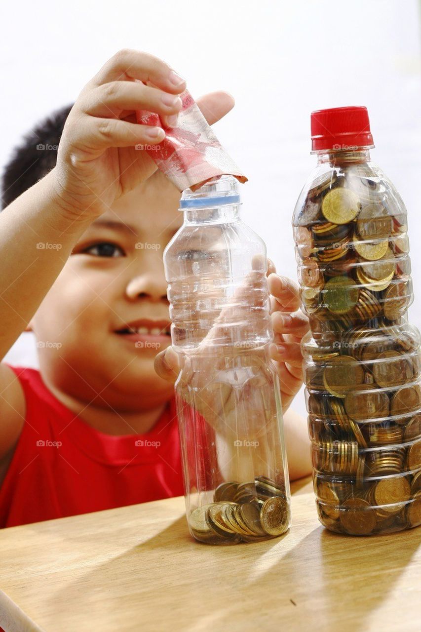 Little boy putting money in a bottle