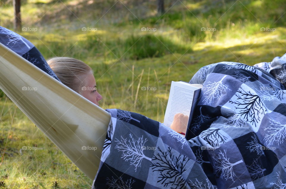 Woman reading book while lying on hammock