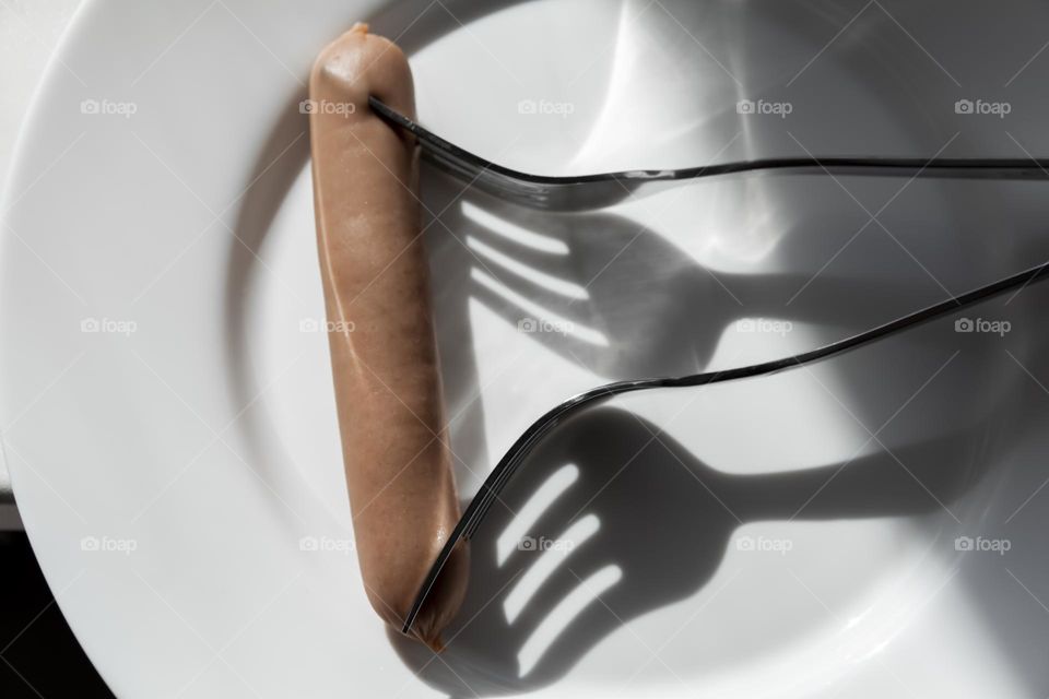 Two forks prick one sausage on a white porcelain plate.