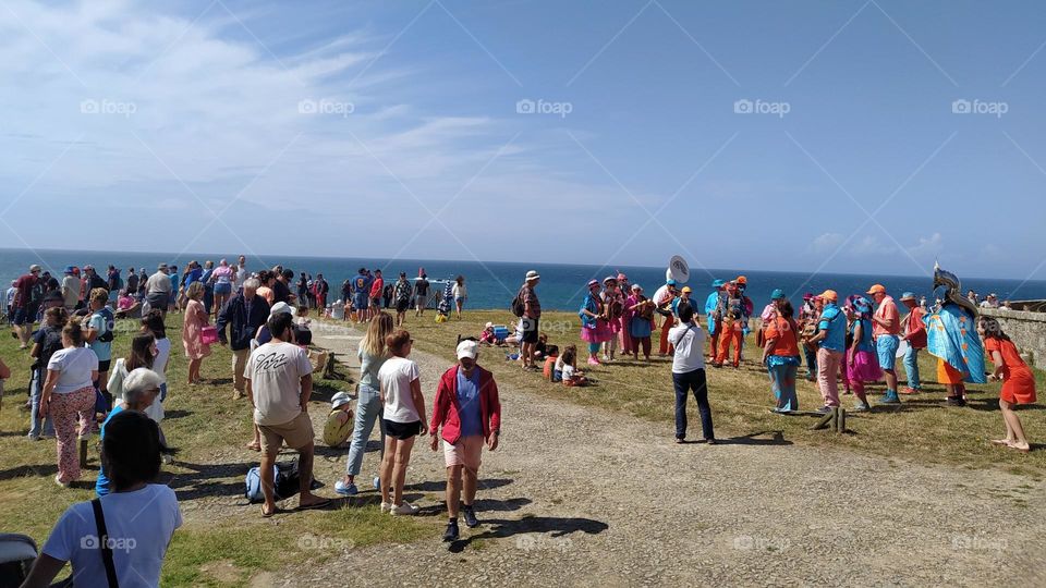 A crowd of spectators and a marching band await runners at the finish of a seaside trail.