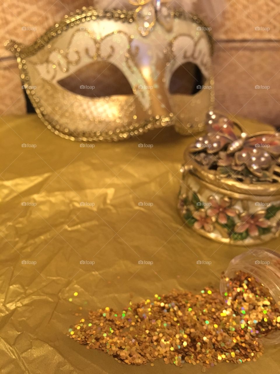 Gold glitter spilled onto tissue paper with a butterfly trinket box and gold Venetian masquerade mask 