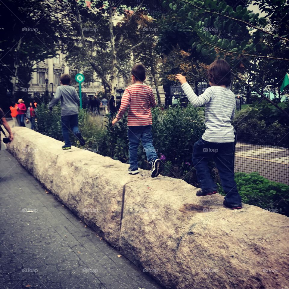 Three boys walking on a ledge in New York City park 