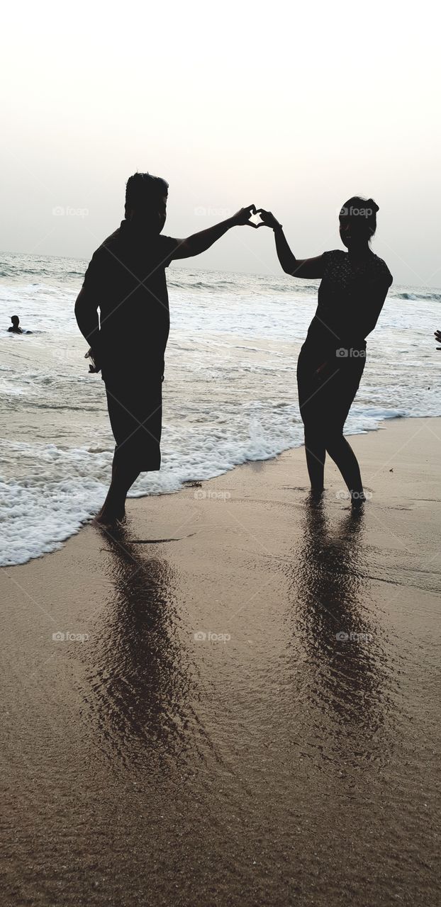 couple covering sun in heart shape on beach