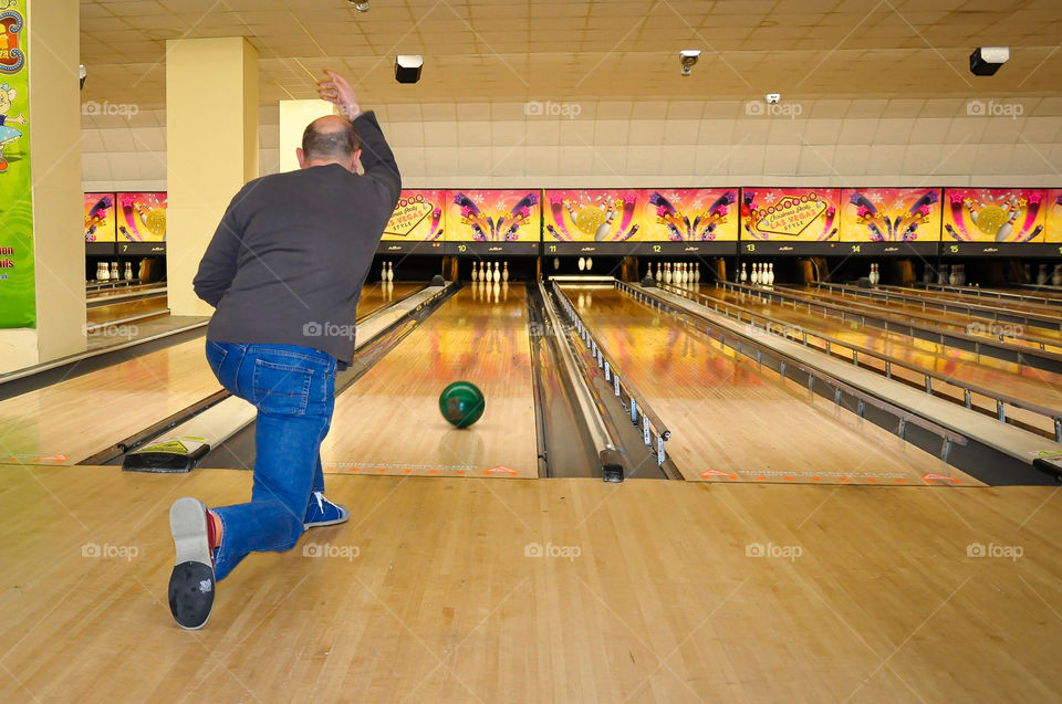 Player rolls a bowling ball towards pins in order to knock all of pins down. Bowling.