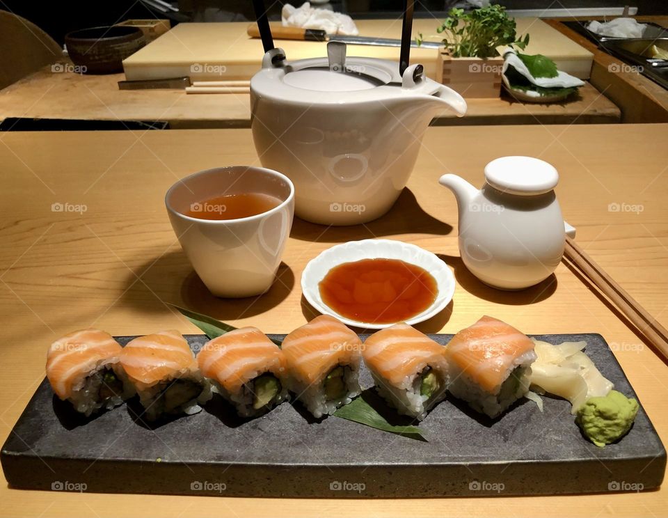 Salmon sushi served on japanese black ceramic dish with jasmine tea and soy sauce in the background 