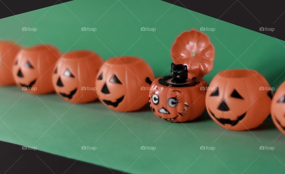 A row of plastic pumpkins, one with a black cat against a green and black background 