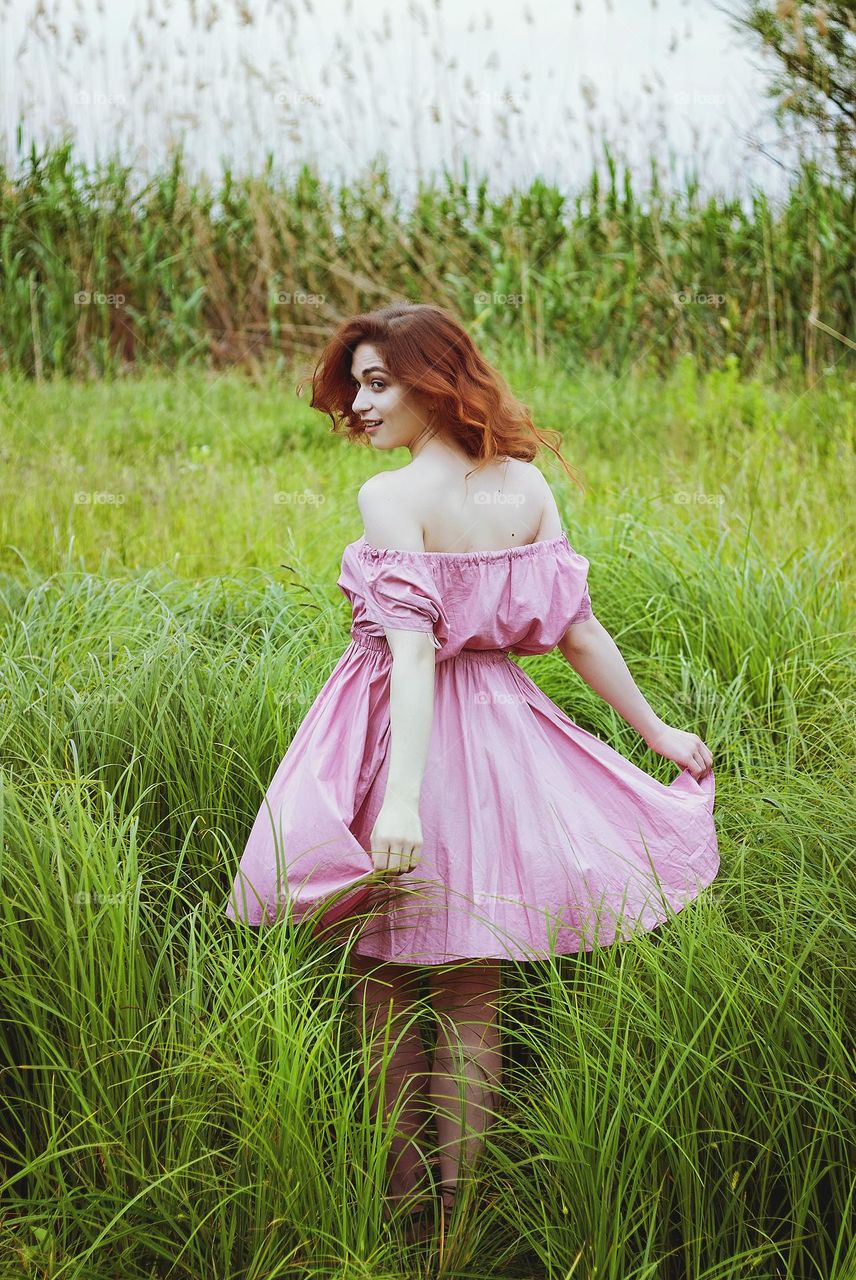 Portrait of beautiful young redhead woman, girl in pink dress sitting  outdoor, in the summer park, meadow with green grass