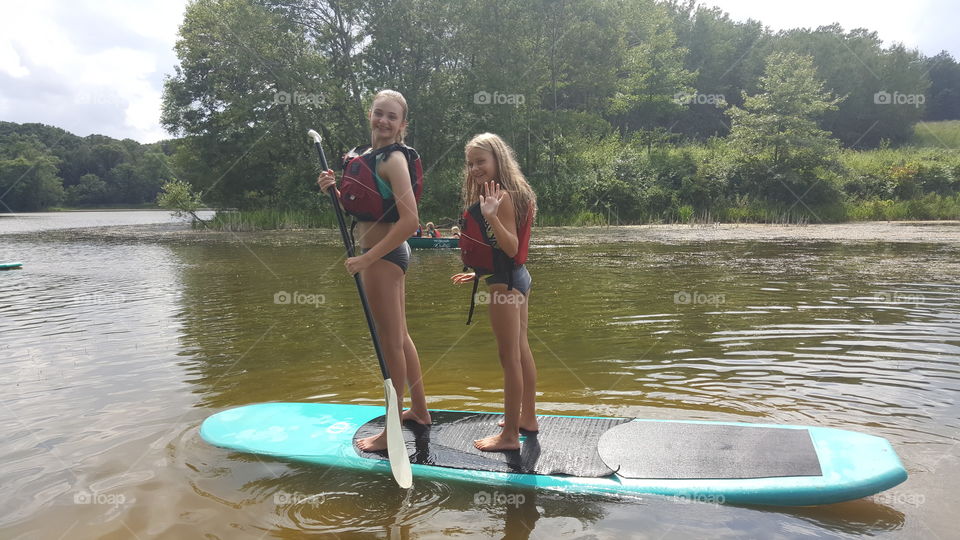 Two sisters paddling with surfboard on river