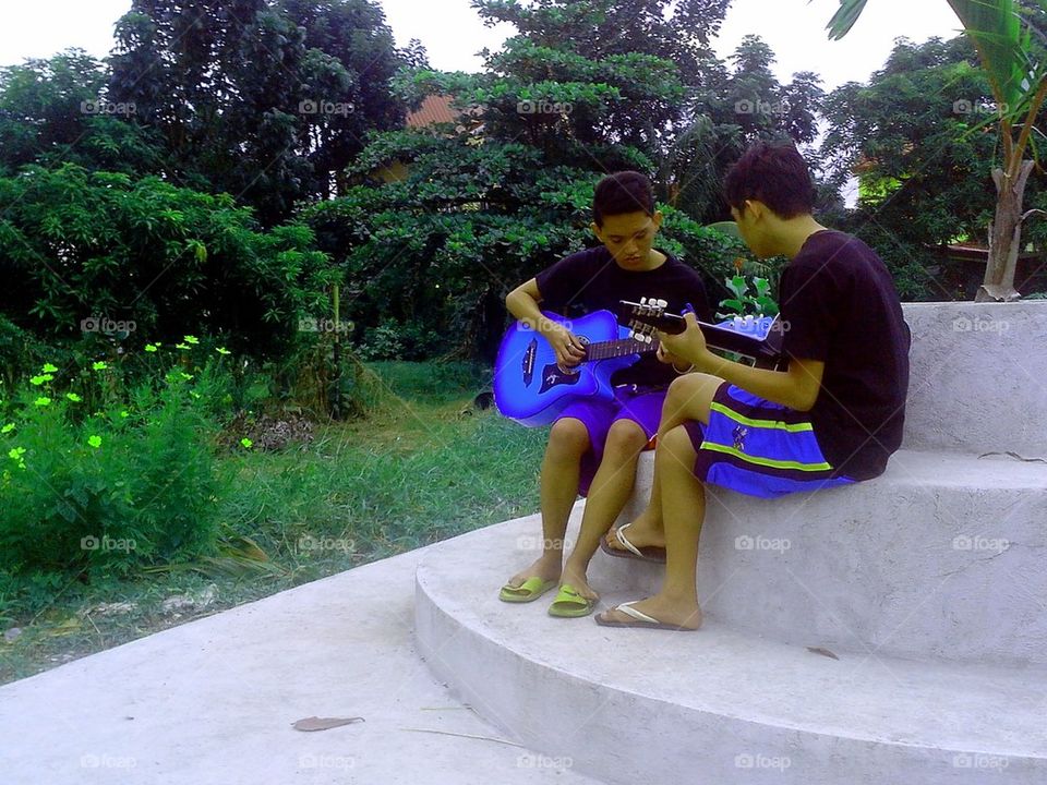 Two boys playing the guitar in a park