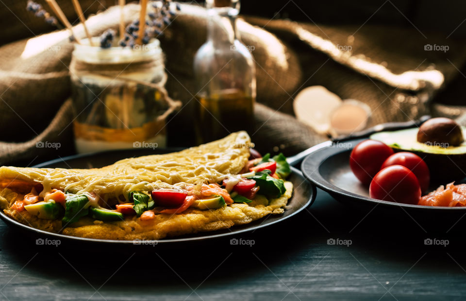 fresh, fluffy omelette with salmon, tomatoes, avocado, cheese and rucola, on a wooden rustic table