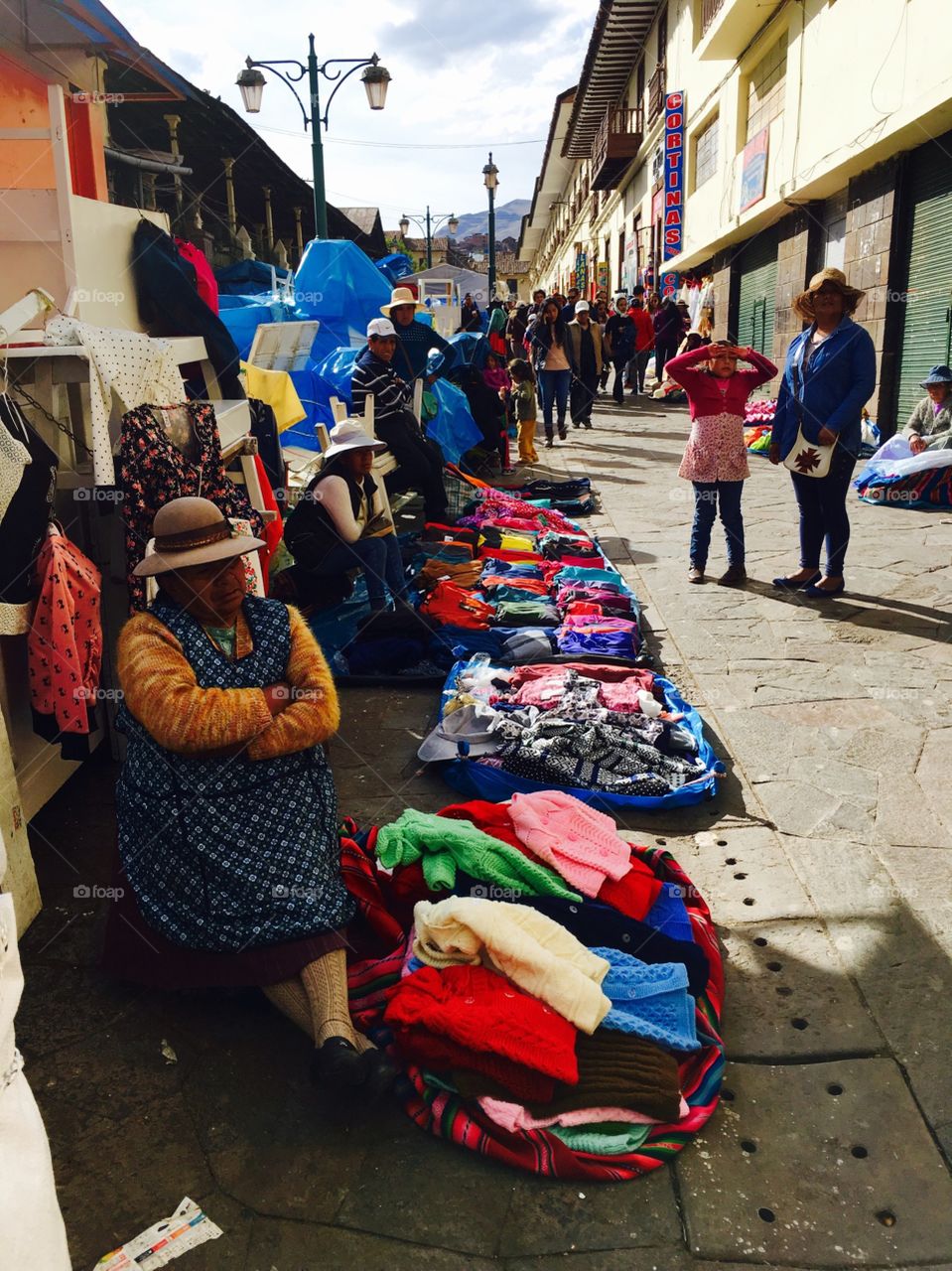 Women set up shop along a street in Cuzco, selling colorful wares such as tapestries and clothing. 