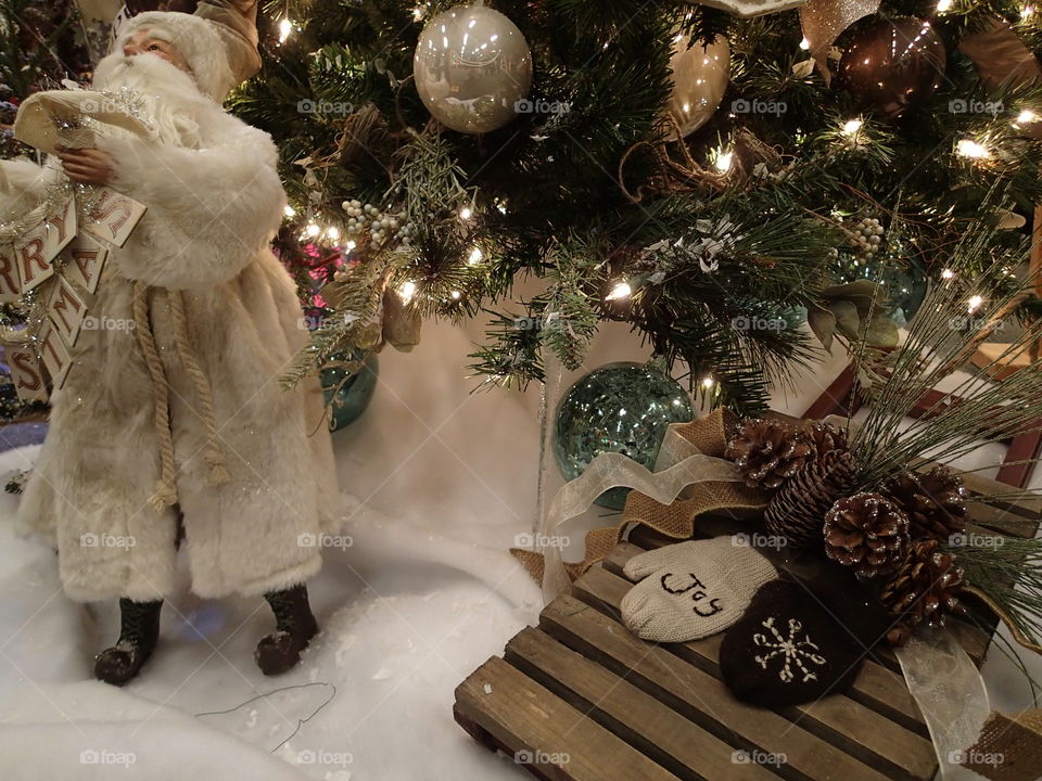 A white robed Santa Claus at the base of a Christmas tree. 