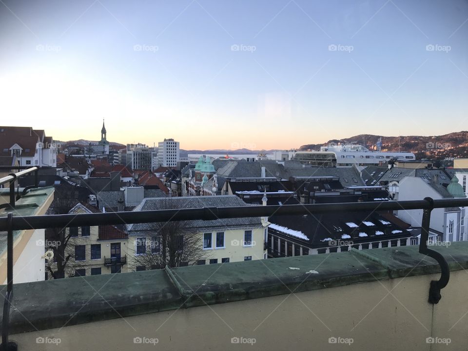 Sunset in Bergen, Norway. The sky is clear, and the orange sunset fades into the blue sky. No clouds in Bergen. The roofs of the city shows way to the sunset. One of the church towers in Bergen shows clearly in the background.