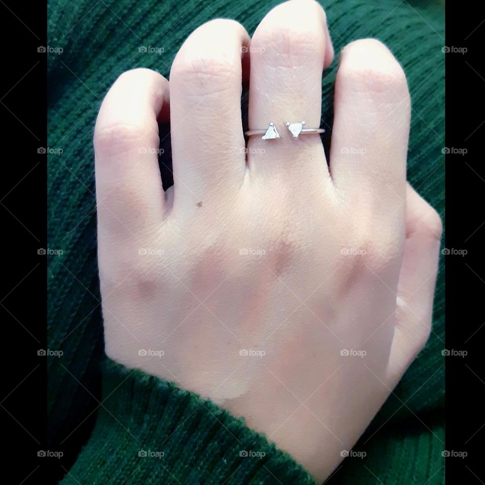 Close up of beautiful white gold ring on the woman finger against green background