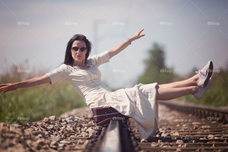 Woman sitting on rail track with suitcase