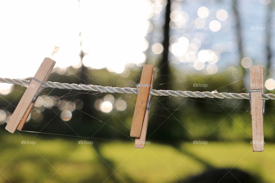 Bokeh effect created by lake background; artistic imagery: three wood clothepins clothes pegs on white rope line outdoors 