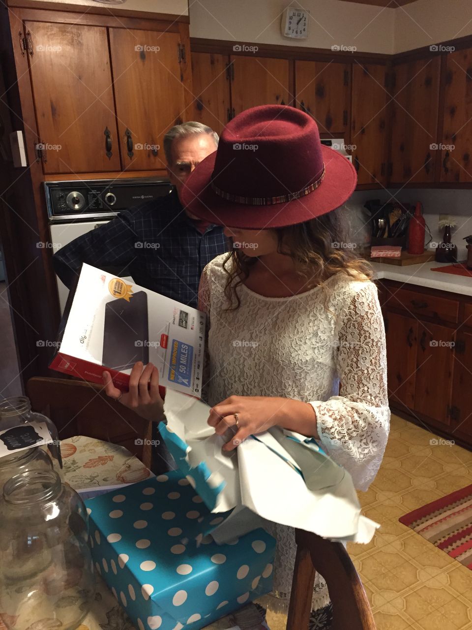 Young lady decked out in maroon hat cream dress, opening a gift.