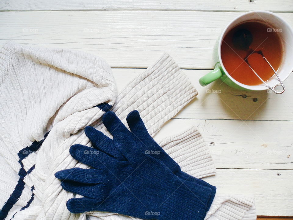 white sweater, blue gloves and cup of tea on white boards