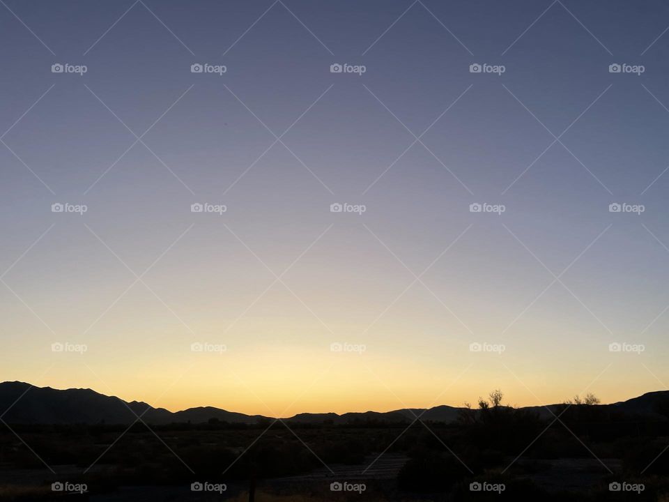 A yellow sunset with mountains and a gray purple above.