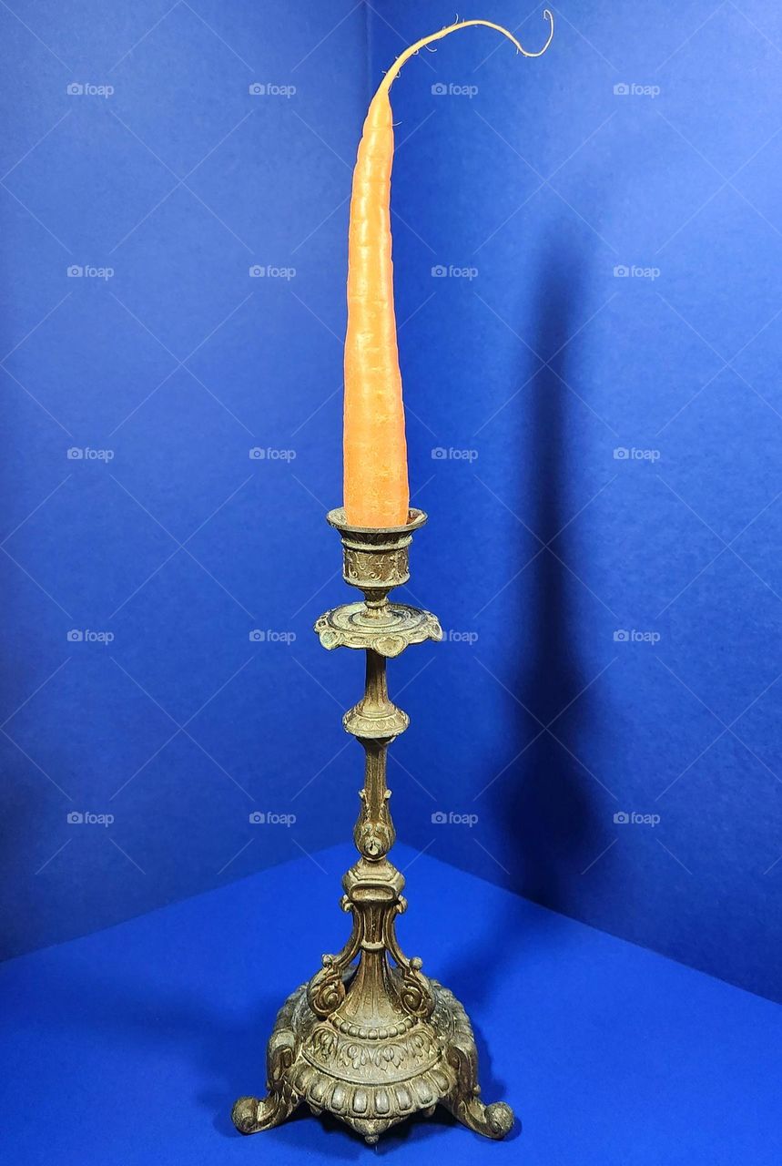Orange and blue complementary colours composition made with a carrot on a vintage candle holder surrounded by blue surfaces