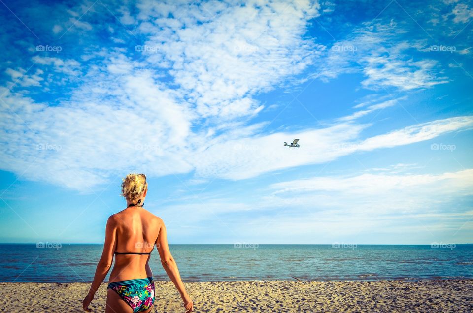 A woman on the beach spots a biplane fly by