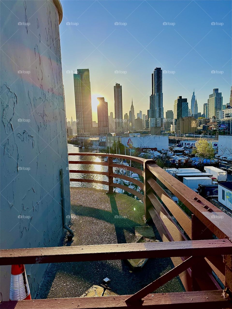 This is the central outpost of the “Pulaski Bridge” at “Newtown Creek” that connects LIC, Queens to “Greenpoint”, Bklyn with a view of LIC and “Manhattan” incl. the “Empire State Bldg” in the warm evening sun. 2024. Hypnotic Productions