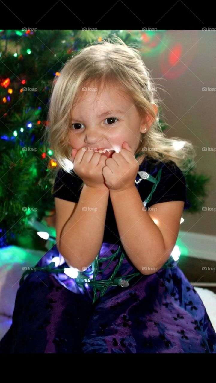 Little girl in front of Christmas tree wrapped in lights
